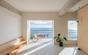 Modern residential interior featuring wooden furniture and floor, with a view of the ocean and clear sky.