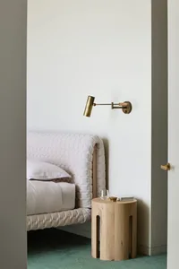 A minimalist bedroom featuring a bed with a quilted headboard, a bedside table made of light-colored wood, and a wall-mounted