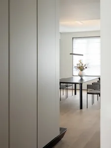 A modern minimalist dining room with wooden flooring, featuring a sleek, black dining table and chairs, and a hanging linear 