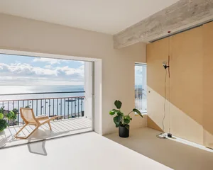 Modern, minimalist interior design featuring concrete walls, floor-to-ceiling windows, and a balcony overlooking the sea.