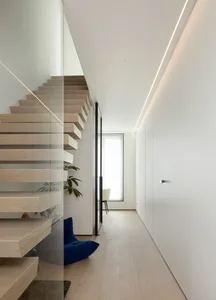 A modern interior design with white walls and wooden stairs and a blue cushion on the floor.