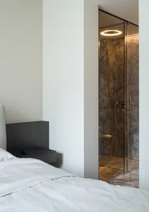 A white minimalist bedroom with a marble shower enclosure and a minimalistic headboard.