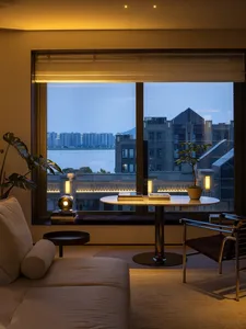 A living room with a sofa, table, and plants, overlooking a cityscape at dusk.