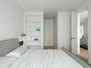 A minimalist bedroom with white furniture, wood accents, and white walls.
