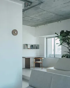 Minimalist residential interior with exposed concrete ceiling, wooden furniture, and a green plant.