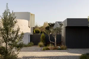 Modern minimalist house featuring concrete and metal exteriors, with landscaping and a patterned driveway.