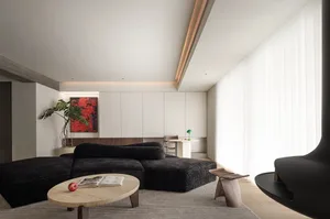 A minimalist living room with a black upholstered sofa, a wooden coffee table, white cabinetry, and glass panel drapes.