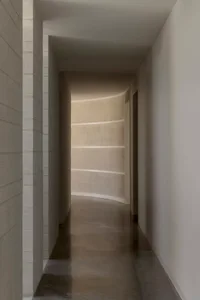 A modern concrete corridor with curved walls leading to a light source at the end.