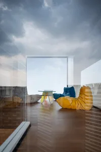 Modern living room featuring a large window with a view of the sky, wooden flooring, and colorful bean bag seating.