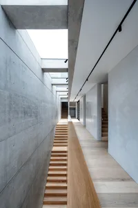 Modern corridor featuring concrete walls, wooden floors, and a wooden staircase.