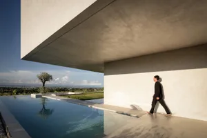 A man walking along a minimalist concrete pool side walkway with a stunning outdoor view.