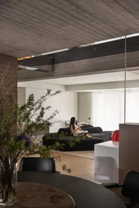 A modern interior living room with a concrete ceiling, black furniture, and a woman sitting on a couch.