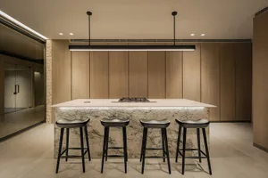 A modern kitchen with wooden cabinets, marble countertops, and black stools.