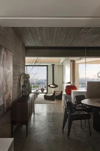 A modern living room with concrete walls and wooden flooring, featuring a hanging fireplace and large windows overlooking a c