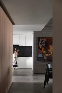 A modern minimalist kitchen with concrete walls, featuring sleek white cabinets and black countertops.