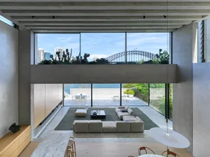 Modern minimalist living room featuring concrete walls and floor-to-ceiling windows overlooking the cityscape and waterfront.