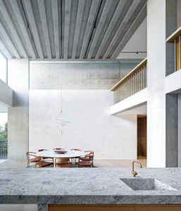 A modern dining room featuring a circular marble table surrounded by orange chairs, set against a concrete wall and illuminat