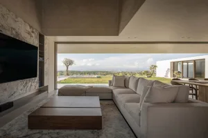 Modern living room with concrete walls and a view of the outdoor landscape, featuring a large sectional sofa and a low coffee