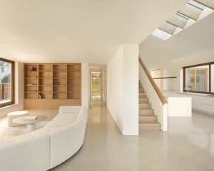 Modern minimalist living room with white couch, wooden bookshelf, and concrete flooring.
