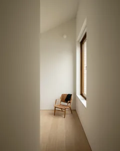 A minimalist bedroom with a wooden chair and a window.