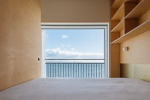 A minimalist bedroom featuring a large window with an ocean view, wood walls, and a bed.
