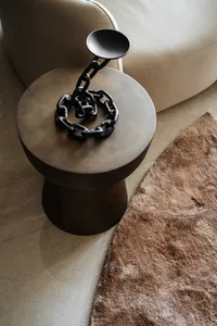 A modern side table with a black metallic chain decorative piece on top, sitting next to a beige leather sofa on a brown text