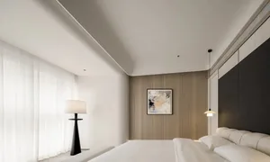 A minimalist bedroom with a white bed, a large window with sheer curtains, and an abstract painting on the wall.