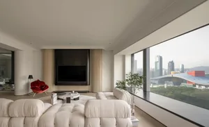 Modern living room with a neutral color palette, featuring a comfortable seating area, a flat-screen TV, and large windows wi