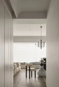 A modern living room with a white interior featuring a round black table, a sleek upholstered chair, and a minimalist chandel