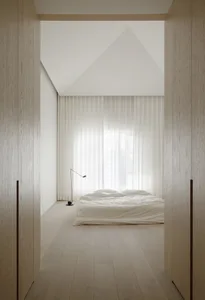 A minimalist bedroom with a bed, lamp, and sheer curtains.