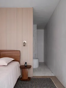 A minimalist bedroom featuring a wooden bed and side table with a modern light fixture.
