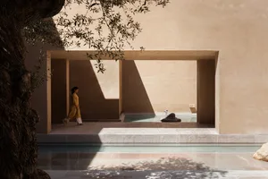 A minimalist architectural landscape featuring sandstone walls and an open space with a pool and sculpture.