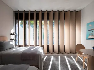 A modern bedroom featuring a bed with white sheets, a wooden headboard, and a large window with wooden blinds.