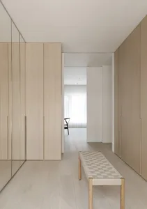 A modern closet interior with light-colored wooden cabinets and a woven seat bench in a minimalist design.
