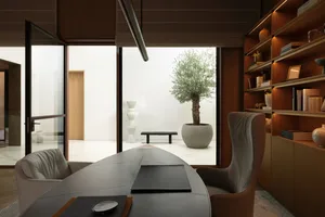 Modern home office with wooden shelves, glass desk, and olive tree in a large planter.