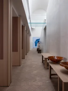 A modern interior design with concrete walls, wooden benches, and glass partitions in a long hallway-like space.