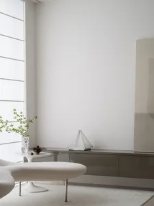Modern minimalist living room featuring white furniture, a sleek glass cabinet, and a white ottoman with a white vase contain