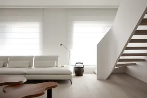 A modern minimalist living room with white furniture and wooden stairs.