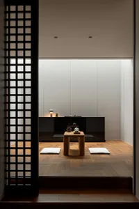 A minimalist living space featuring a wooden column table, white cushions, and a black cabinet with a light fixture.