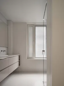 A minimalist white bathroom with a sleek design, featuring white walls, ceiling, floor, and a large rectangular window with b