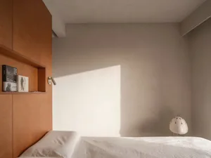 Minimalist bedroom featuring a white sheet-covered bed with a wooden headboard and a white floor lamp.