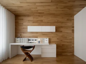 A minimalist office with a wooden desk, chair, and cabinet against a backdrop of wooden paneling.