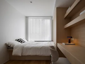 A modern bedroom featuring white bedding on a wooden bedframe, with a small table and chair by the window.
