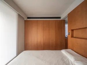 A minimalist bedroom with a white bed and wooden paneled walls.