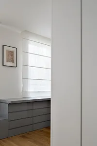 Modern gray kitchen cabinets situated by a window sill with sheer white curtains.