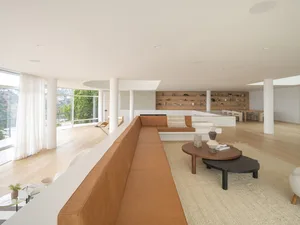 Modern living room featuring a long brown leather sofa, wooden flooring, and white walls.
