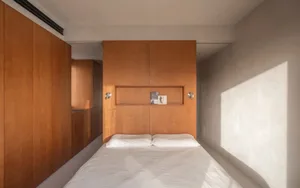 A modern minimalist bedroom with concrete walls and a wooden headboard, featuring a clean and organized space.