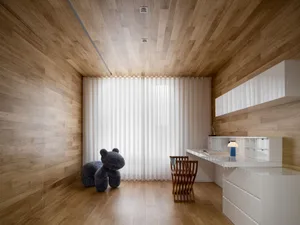 Modern minimalist home office with wooden floor and walls, featuring a white desk and chair, and a plush toy horse.