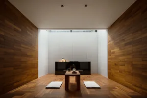 A modern minimalist living room featuring wood flooring, a low table, and cushions.