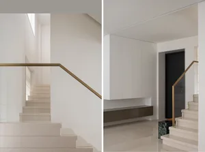 Modern white concrete staircase with gold aluminum railings and black door in an interior space with minimalist design elemen